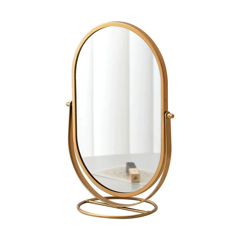 A round, gold-toned rotating oval vanity mirror with a thin frame.