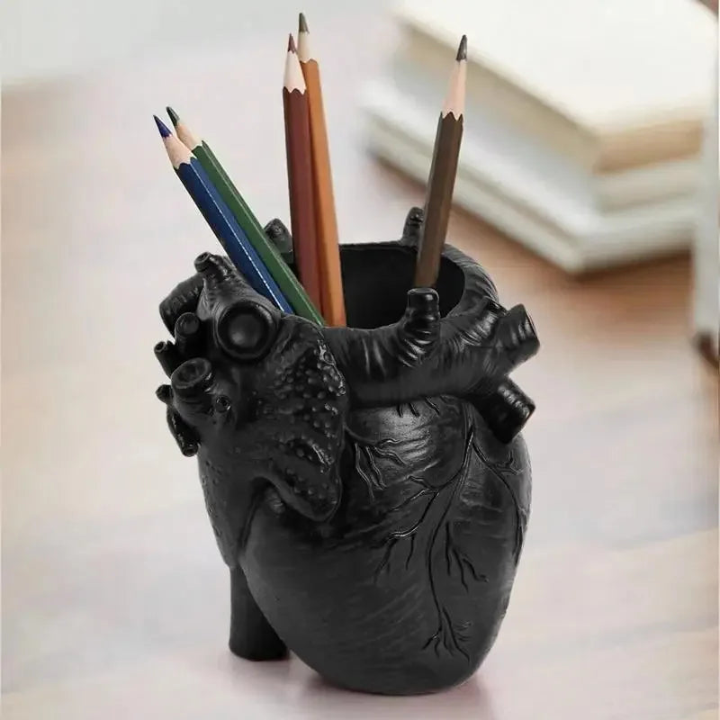 A black heart-shaped resin organizer holds several colored pencils and a paintbrush.