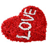 A heart shape made of red rose petals with white lettering on it.