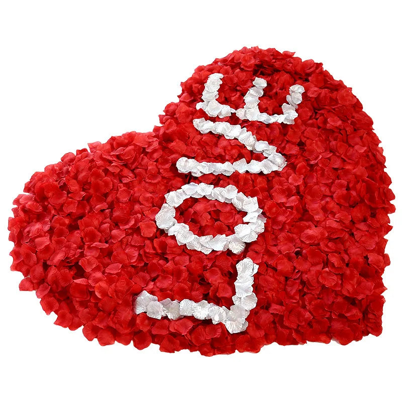 A heart shape made of red rose petals with white lettering on it.