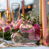 Herzförmige Acrylplatte mit eingraviertem Text inmitten von rosa und grünen Blumenarrangements.