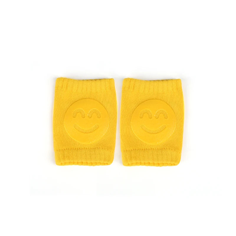 A pair of bright yellow knitted knee pads for crawling infants, each featuring a smiling face.
