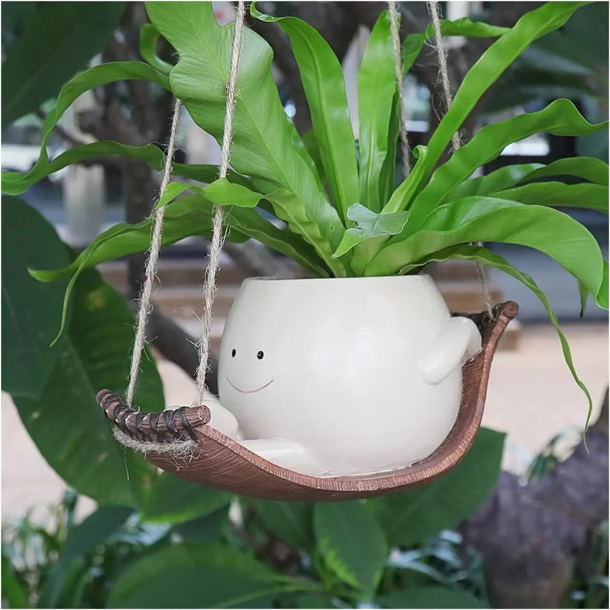 A white ceramic ornament shaped like a smiling face is hanging from a plant vine.