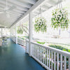Two hanging floral decor arrangements featuring white flowers and green eucalyptus on a porch walkway.