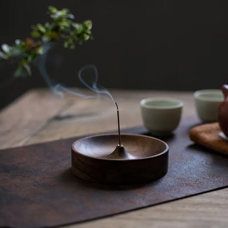 A dark wooden incense stick burner with a thin stick emitting smoke on a slate surface.