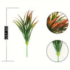 A tall, vibrant green artificial grass plant with reddish-brown tips and tropical flowers.