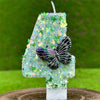 A number four candle decorated with green sequins and a butterfly design, set on a wooden surface.