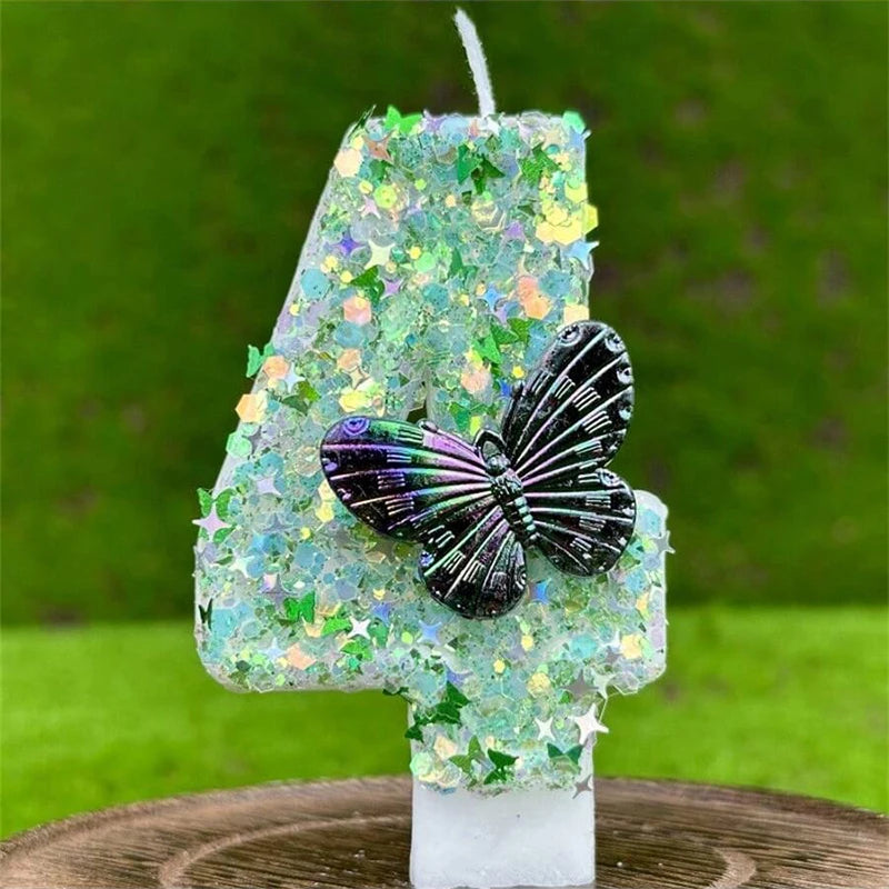 A number four candle decorated with green sequins and a butterfly design, set on a wooden surface.