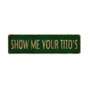 A rectangular, dark green metal sign with the text SHOW ME YOUR TITO's engraved on it.