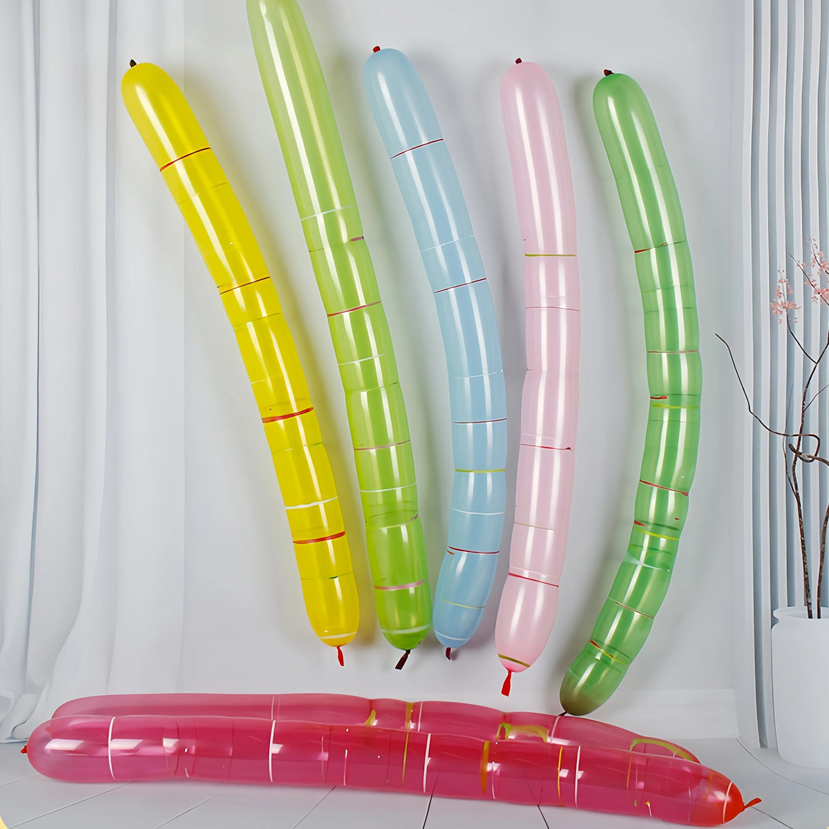A collection of colorful, elongated balloon strips in yellow, green, blue, and pink are displayed against a white background.