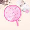 Pink portable foldable cooling handheld fan with a floral pattern resting on a light background.