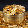 A pile of small gold bars is displayed in a metal container on a bed of similar gold pieces.