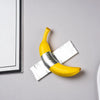 A yellow banana sculpture is shown resting on a silver-wrapped piece of paper against a light gray background.