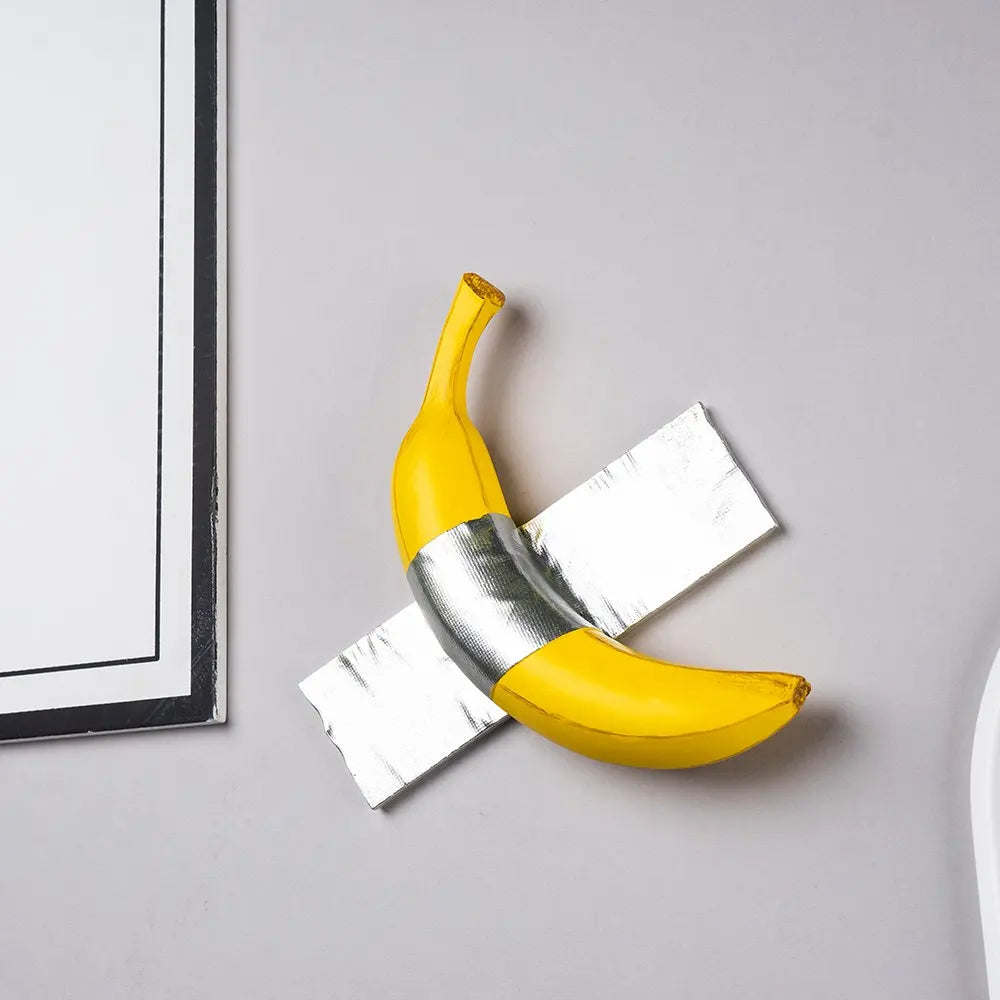 A yellow banana sculpture is shown resting on a silver-wrapped piece of paper against a light gray background.