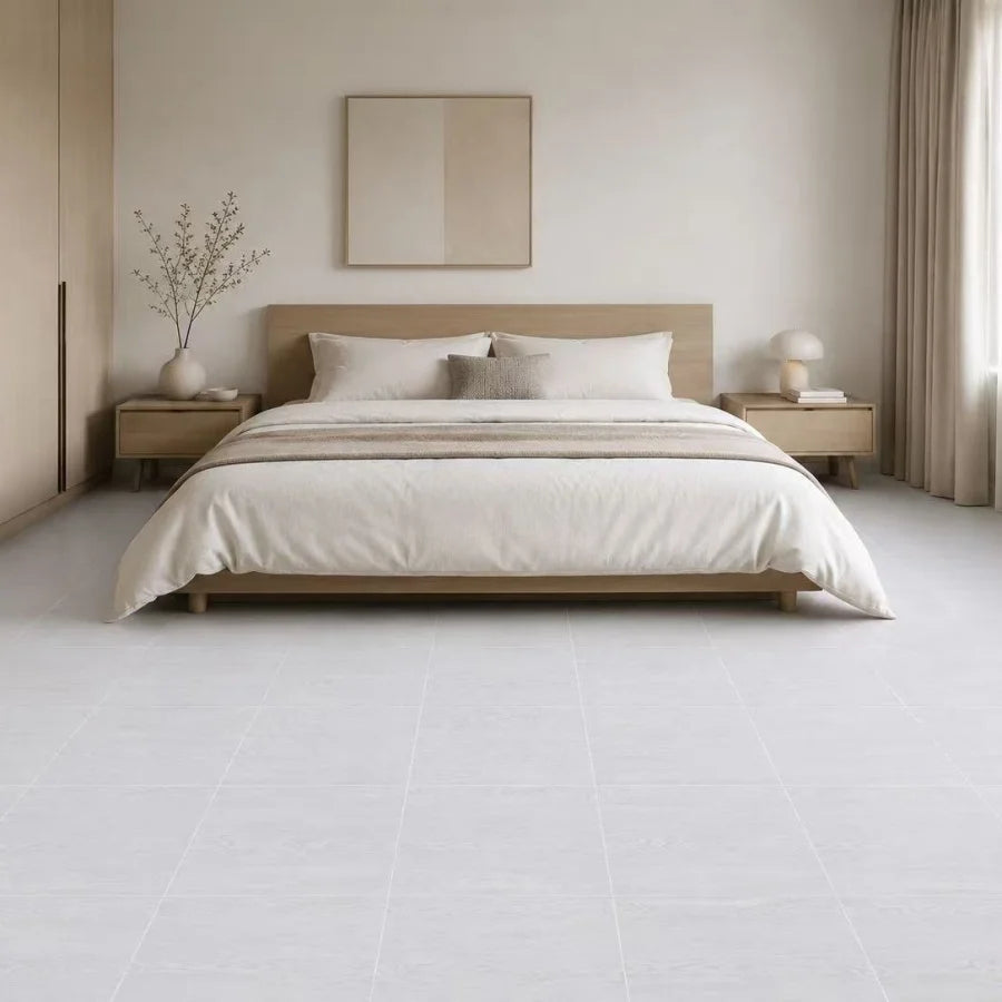 A minimalist bedroom featuring a wooden bed frame, light neutral bedding, and pale tiled floor.