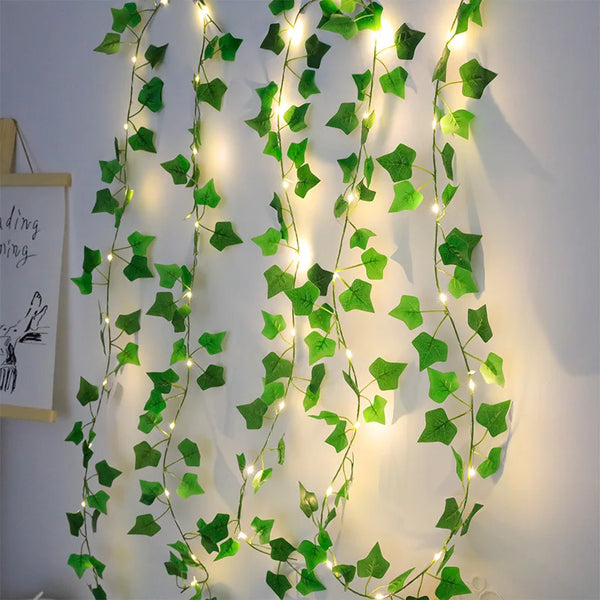 Green leaf string lights with ivy vine decoration illuminating a white wall.