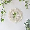Miroir macramé rond avec frange beige naturelle, entouré de lierre vert.