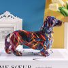 A colorful resin figurine of a dachshund dog in various vibrant colors standing on a white box.