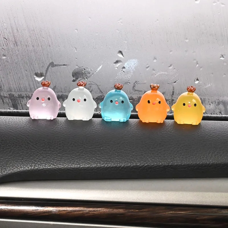 Five luminous resin chicken car ornaments in pink, white, blue, orange, and yellow sitting on a dark surface.