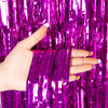 A hand holds purple metallic tinsel foil fringe curtain backdrop for parties.