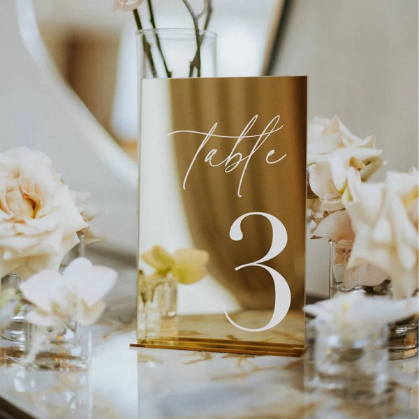 Número de mesa de acrílico espejado dorado elegante con el número tres sobre un fondo claro