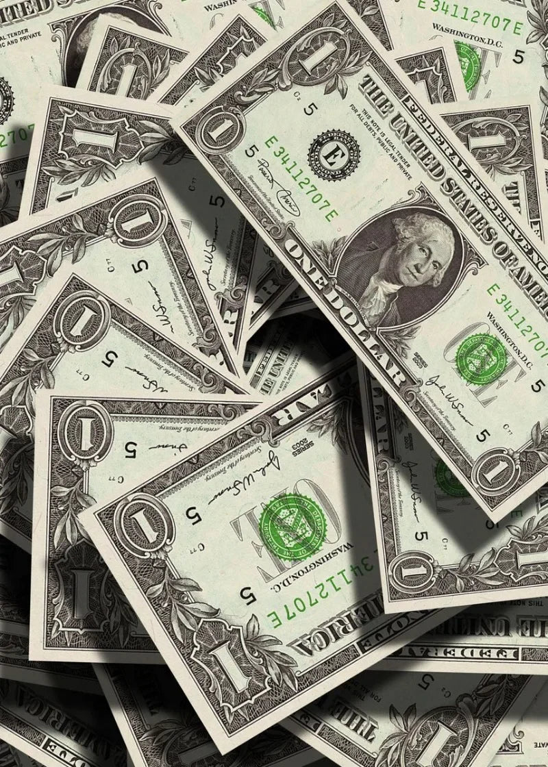 لقطة مقربة لعدة أوراق نقدية بالدولار الأمريكي مبعثرة ومتداخلة، تُظهر تفاصيل وظلال دقيقة.