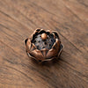 A small, bronze-colored vintage alloy incense burner holder with a flower-like design sits on a dark wooden surface.
