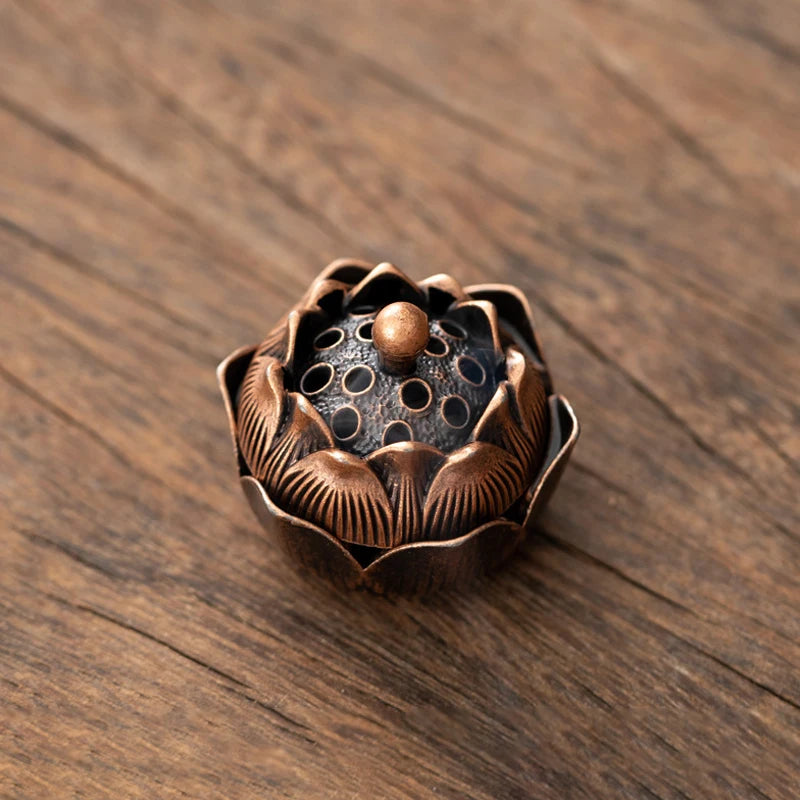 A small, bronze-colored vintage alloy incense burner holder with a flower-like design sits on a dark wooden surface.