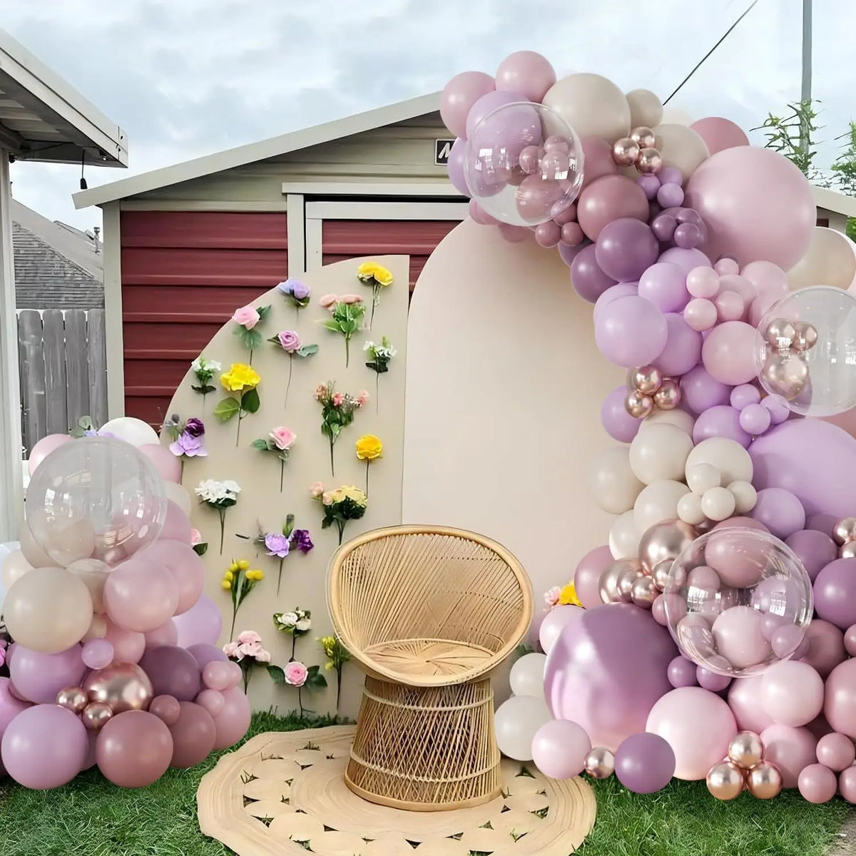 A large balloon arch display featuring pink and purple latex balloons set up outdoors on a green lawn.