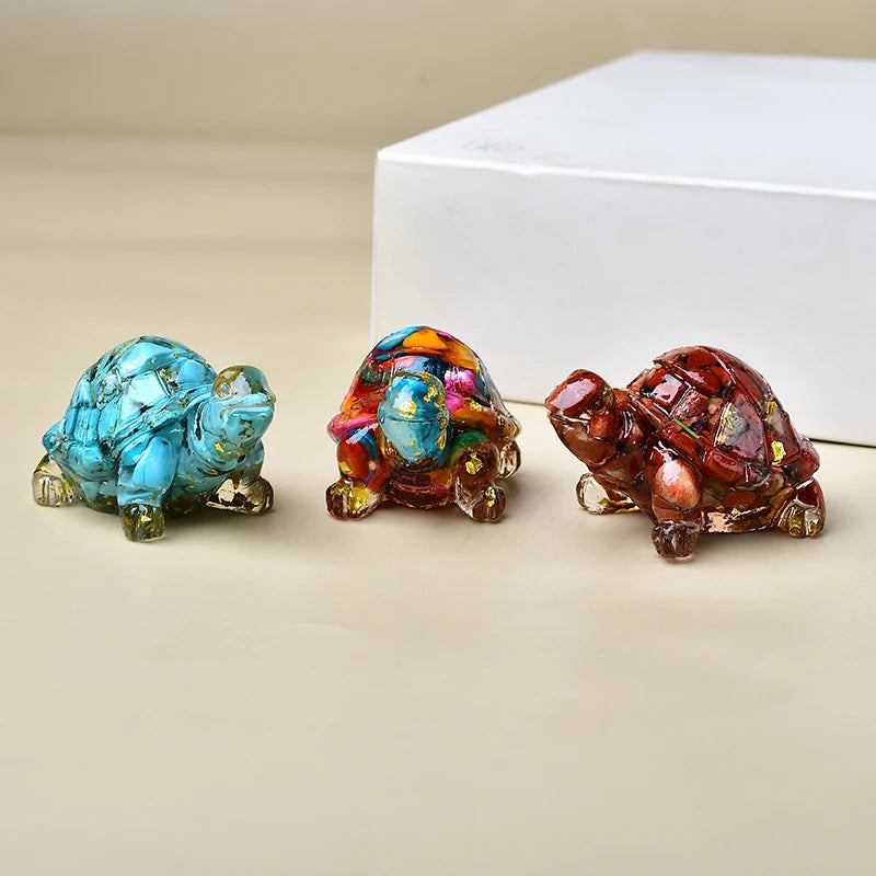 Drei Kristall-Schildkrötenfiguren in Blau-, Violett- und rötlich-braunen Tönen auf einer hellen Oberfläche.