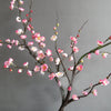 A branch of artificial plum blossoms featuring pink and white flowers on bare branches.