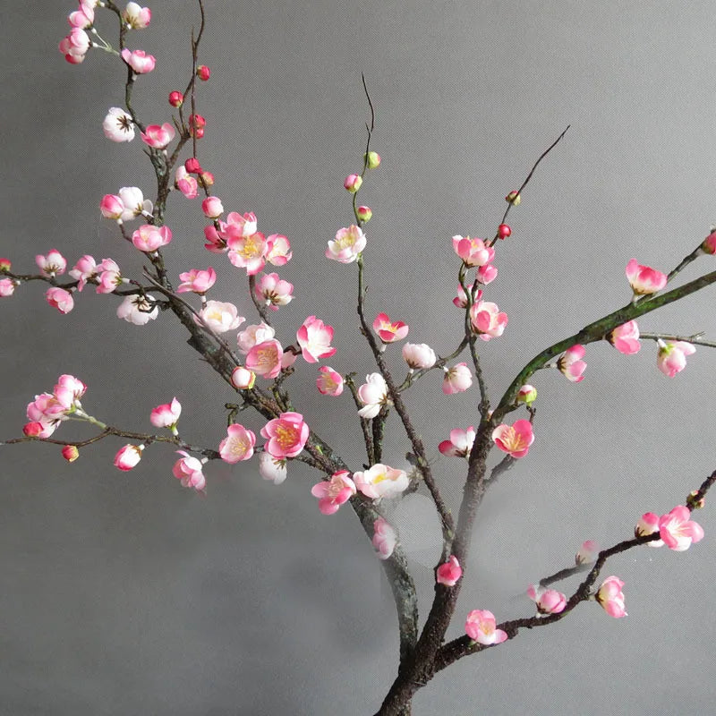 A branch of artificial plum blossoms featuring pink and white flowers on bare branches.
