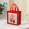A red plaid gift tote bag with a pink Christmas print and red handles, resting on a white cloth.