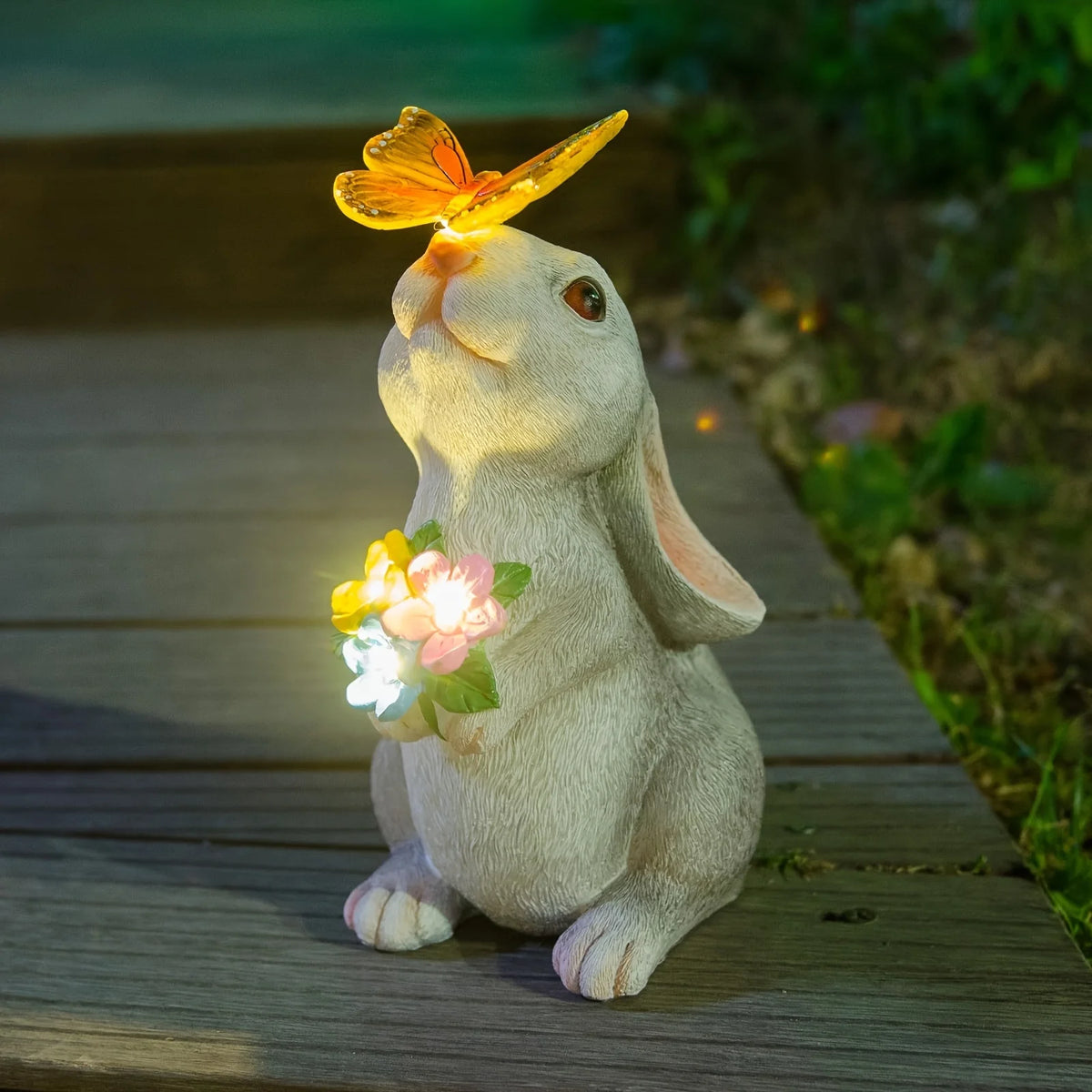 A light-up solar-powered rabbit garden statue with a butterfly perched on its head, sitting on a wooden surface.