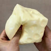 A hand holds a large, pale yellow cheese cube stress ball fidget toy.