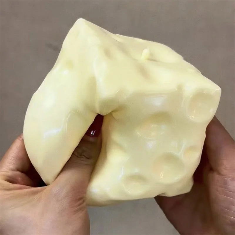 A hand holds a large, pale yellow cheese cube stress ball fidget toy.