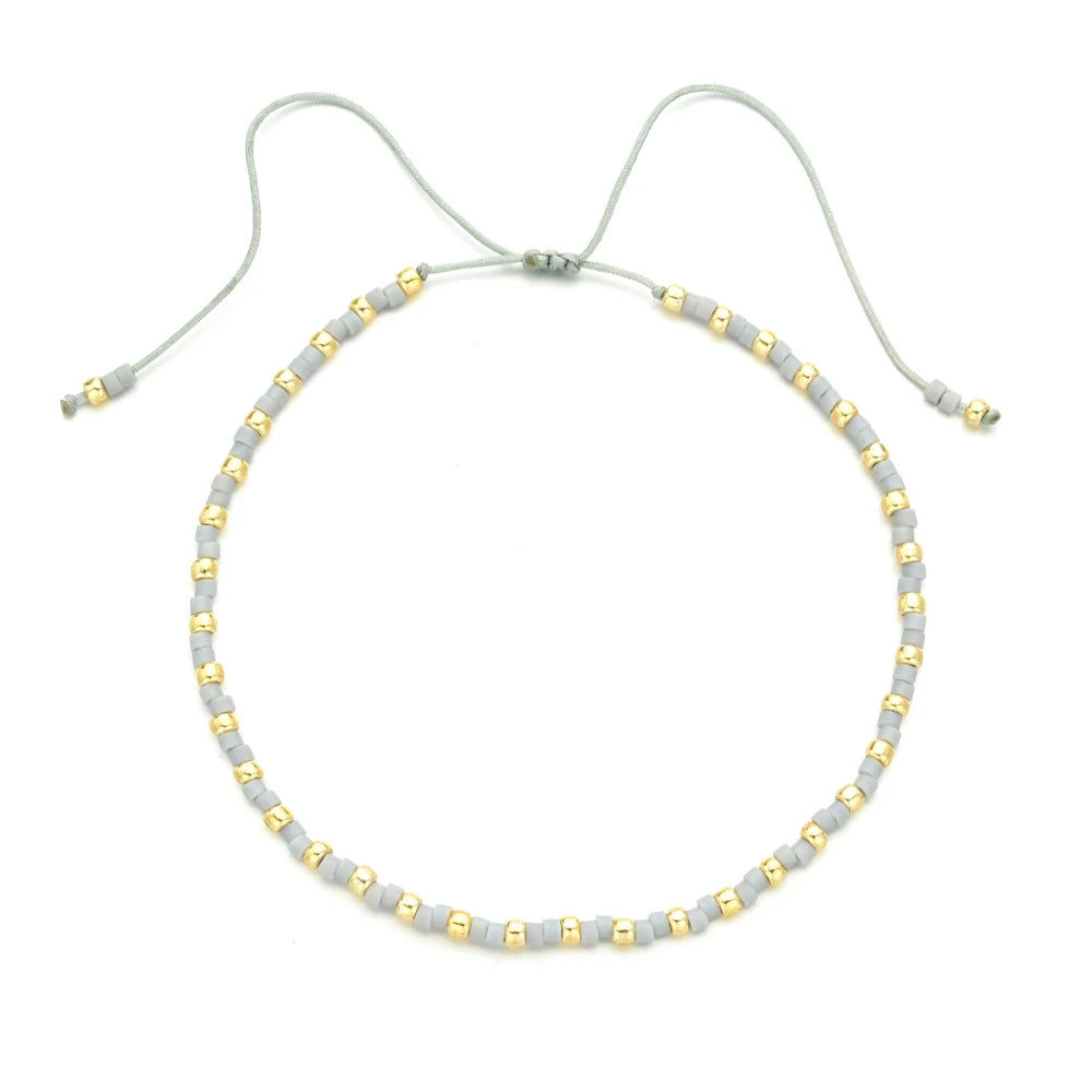 Handmade boho glass bead bracelet with adjustable cord featuring small gray and gold beads.