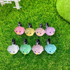 A set of seven small, luminous resin bird fairy garden decor pieces in various pastel colors resting on green moss.