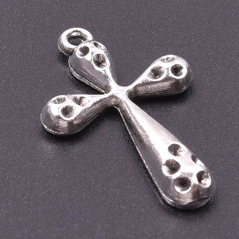 A silver cross charm with a textured surface and a loop, photographed against a dark gray background.