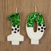 Two white candles shaped like the numbers 1 and 0 decorated with green glitter soccer balls