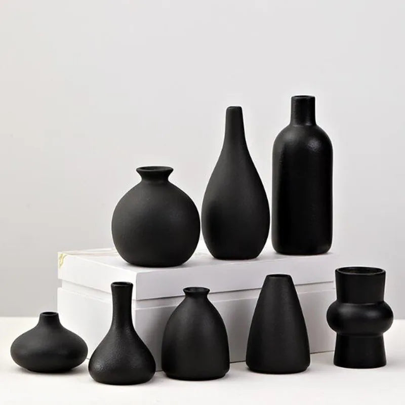 A collection of modern ceramic vases in matte black, including various shapes and sizes, displayed on a white surface.