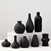 A collection of modern ceramic vases in matte black, including various shapes and sizes, displayed on a white surface.
