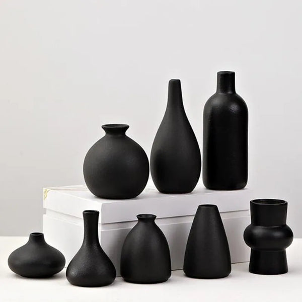 A collection of modern ceramic vases in matte black, including various shapes and sizes, displayed on a white surface.