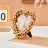 A heart-shaped photo frame made of gold-colored roses surrounds a soft pink floral insert.