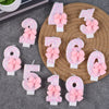 Glitter number candles shaped like 0 through 9 with pink bows arranged on a gray surface.
