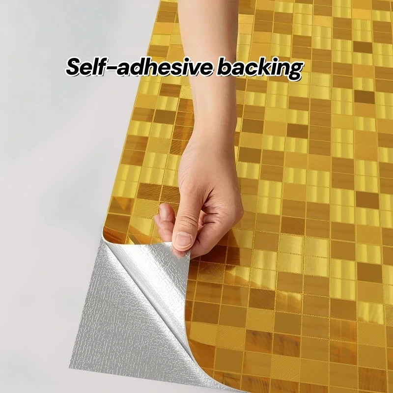 A hand is peeling a strip of metallic gold striped self-adhesive backing from a sheet of gold tiled wallpaper.