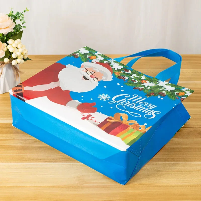 A blue gift bag with a festive Christmas design featuring Santa Claus and greenery, resting on a wooden surface.