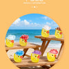 A set of glow-in-the-dark resin duck figurines with colorful hats sitting on a wooden deck near the ocean.