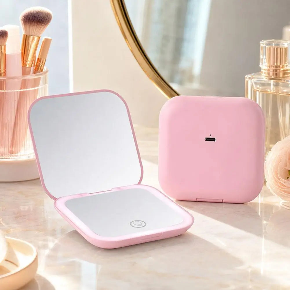 A pink portable folding LED makeup mirror with a reflective surface is displayed on a marble surface.