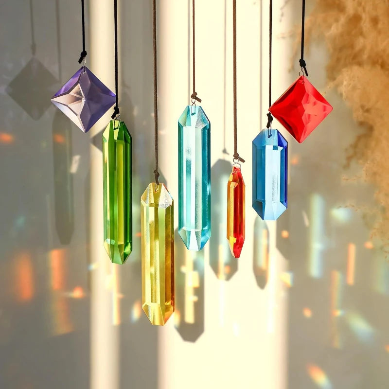 A collection of seven colorful crystal prism sun catchers hanging by thin strings against a bright background.